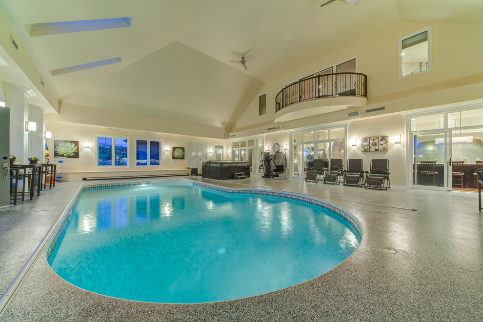 Expansive transitional indoor custom-shaped pool in Calgary with concrete slab.