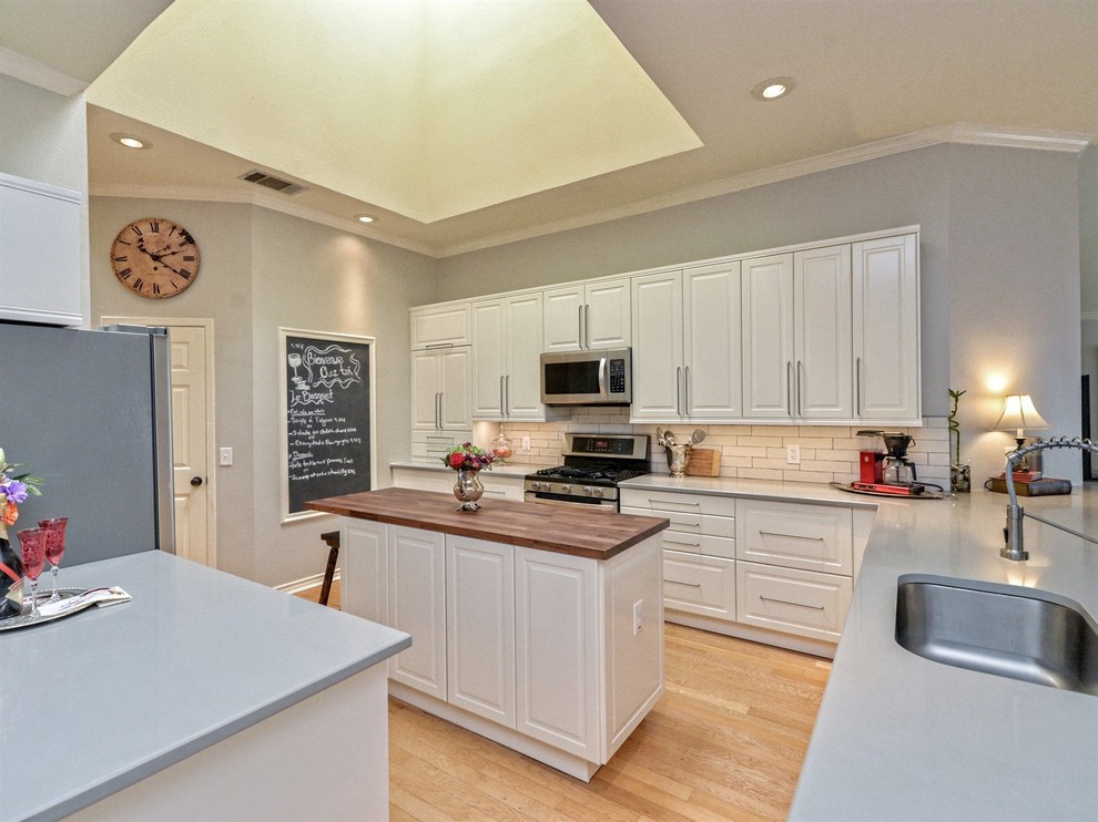 This is an example of a mid-sized traditional l-shaped eat-in kitchen in Austin with an undermount sink, shaker cabinets, white cabinets, quartz benchtops, beige splashback, porcelain splashback, stainless steel appliances, light hardwood floors, with island, brown floor and grey benchtop.