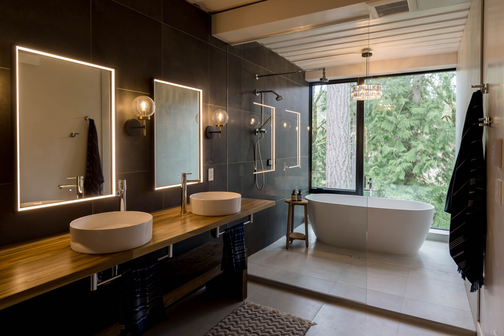 This is an example of a large industrial master bathroom in Seattle with open cabinets, a freestanding tub, an open shower, black tile, black walls, ceramic floors, a vessel sink, wood benchtops, grey floor, an open shower, a double vanity and a floating vanity.