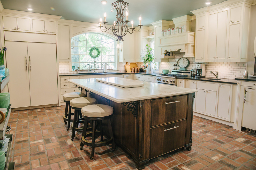 Design ideas for a mid-sized country u-shaped kitchen in Oklahoma City with an undermount sink, flat-panel cabinets, white cabinets, quartz benchtops, white splashback, subway tile splashback, panelled appliances, brick floors, with island, brown floor and white benchtop.