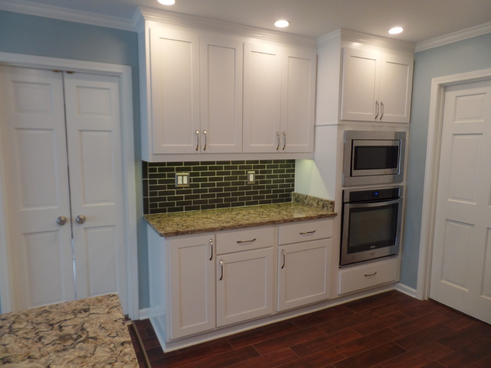 Photo of a large transitional u-shaped eat-in kitchen in Other with an undermount sink, shaker cabinets, white cabinets, quartz benchtops, green splashback, glass tile splashback, stainless steel appliances, porcelain floors and a peninsula.
