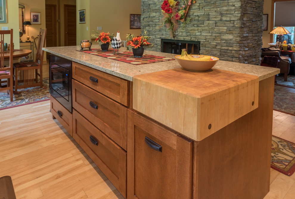 Photo of a large traditional l-shaped eat-in kitchen in Minneapolis with a farmhouse sink, shaker cabinets, light wood cabinets, granite benchtops, beige splashback, subway tile splashback, stainless steel appliances, light hardwood floors, with island, brown floor and brown benchtop.