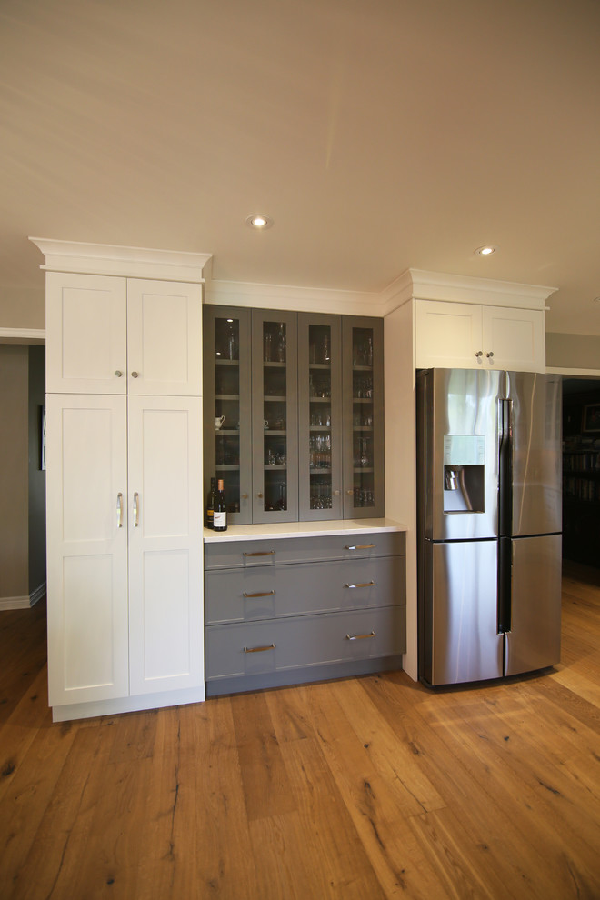 Eat-in kitchen - large transitional l-shaped medium tone wood floor and brown floor eat-in kitchen idea with an undermount sink, shaker cabinets, white cabinets, stainless steel appliances, an island, solid surface countertops and white backsplash