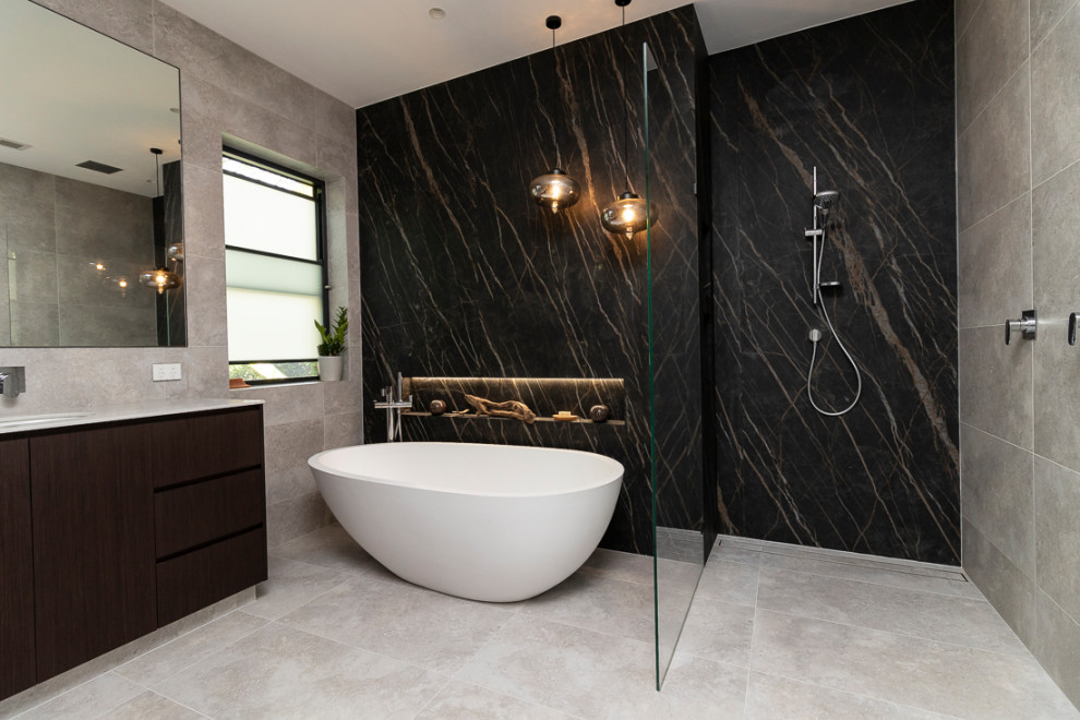 This is an example of an expansive modern 3/4 bathroom in Sydney with flat-panel cabinets, dark wood cabinets, a freestanding tub, an open shower, a wall-mount toilet, gray tile, porcelain tile, multi-coloured walls, porcelain floors, an undermount sink, tile benchtops, grey floor, an open shower and white benchtops.