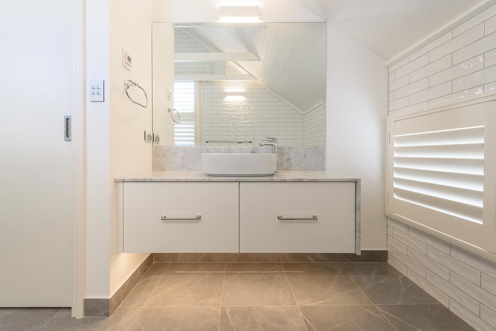 Inspiration for a mid-sized traditional bathroom in Melbourne with flat-panel cabinets, white cabinets, an alcove shower, a two-piece toilet, white tile, ceramic tile, white walls, porcelain floors, a vessel sink, marble benchtops, grey floor and a hinged shower door.