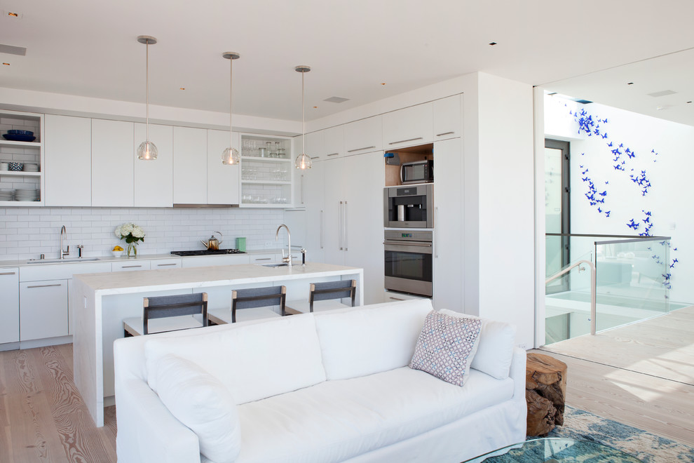 Photo of a contemporary open plan kitchen in San Francisco with an undermount sink, flat-panel cabinets, white cabinets, white splashback, subway tile splashback and stainless steel appliances.