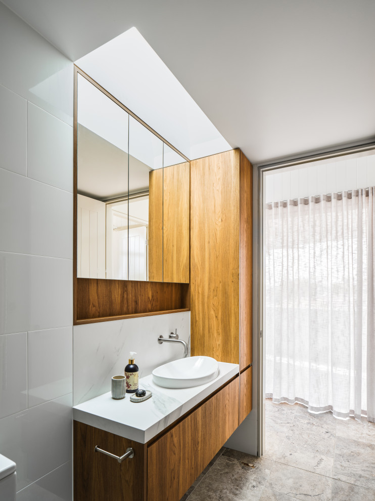 Пример оригинального дизайна: детская ванная комната среднего размера в стиле ретро с фасадами с утопленной филенкой, светлыми деревянными фасадами, душем в нише, инсталляцией, белой плиткой, керамической плиткой, белыми стенами, полом из травертина, накладной раковиной, столешницей из искусственного кварца, бежевым полом, открытым душем, белой столешницей, нишей, тумбой под одну раковину, подвесной тумбой и многоуровневым потолком