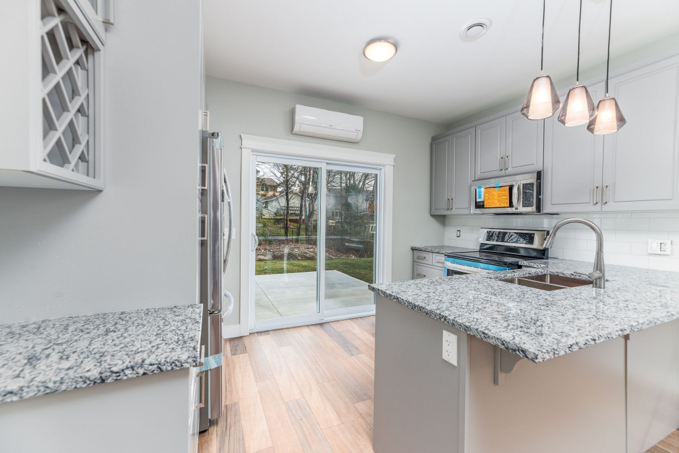 Open concept kitchen - small transitional u-shaped brown floor open concept kitchen idea with an undermount sink, raised-panel cabinets, gray cabinets, granite countertops, white backsplash, ceramic backsplash, stainless steel appliances, a peninsula and multicolored countertops