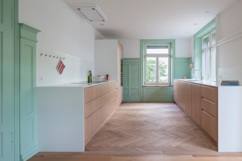 Scandinavian galley kitchen in Other with an undermount sink, flat-panel cabinets, light wood cabinets, panelled appliances and light hardwood floors.