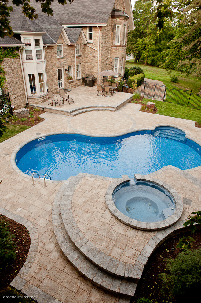 This is an example of a mid-sized country backyard kidney-shaped natural pool in Toronto with a hot tub and natural stone pavers.