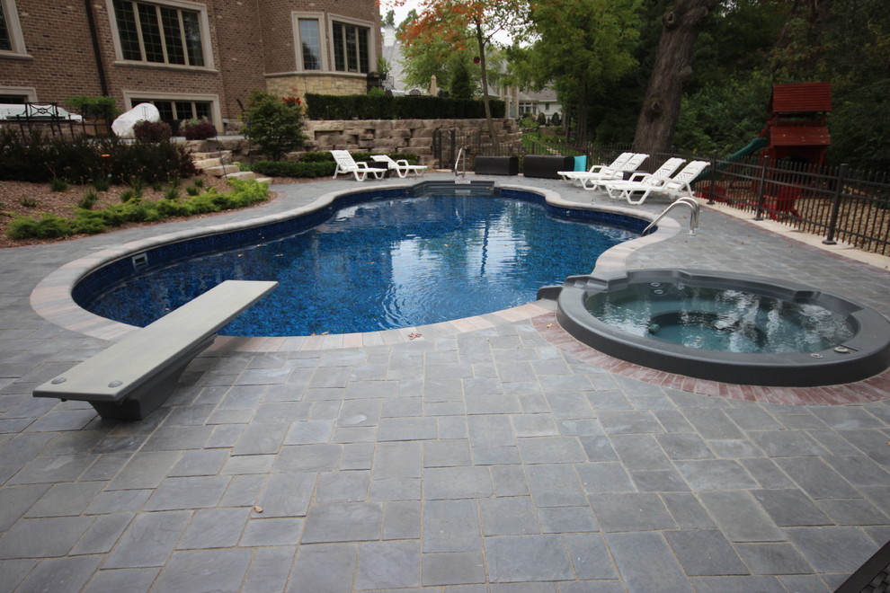 Mid-sized mediterranean backyard kidney-shaped lap pool in Chicago with a hot tub and natural stone pavers.