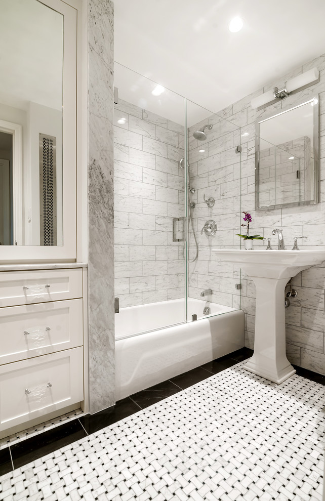 Photo of a small transitional bathroom in New York with recessed-panel cabinets, white cabinets, an alcove tub, a shower/bathtub combo, gray tile, stone tile, grey walls, mosaic tile floors and a pedestal sink.
