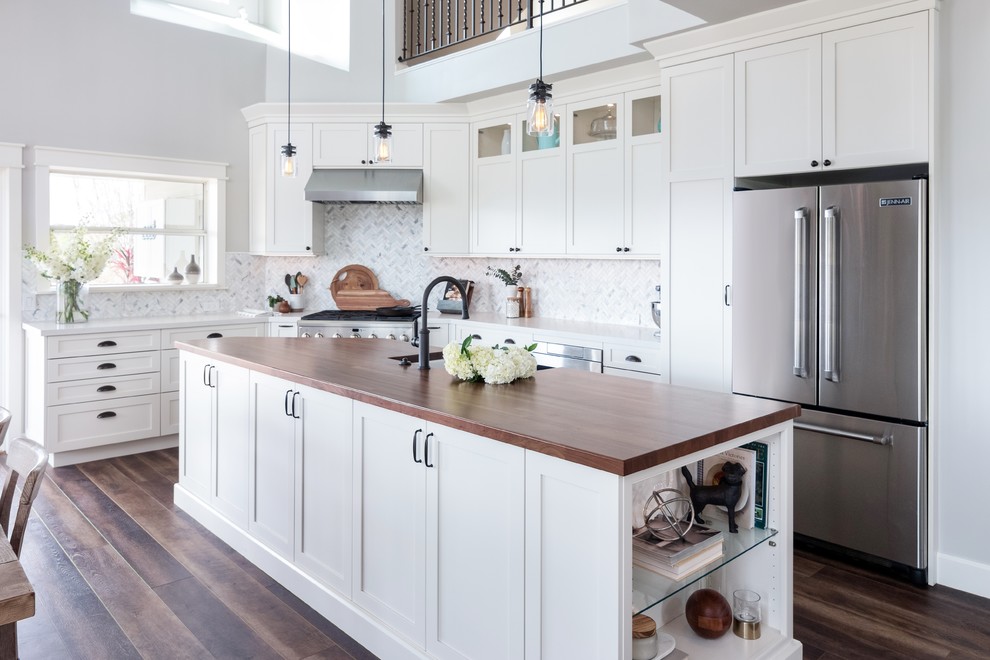 This is an example of a country l-shaped kitchen in Los Angeles with shaker cabinets, white cabinets, multi-coloured splashback, stainless steel appliances, dark hardwood floors, with island, brown floor and white benchtop.