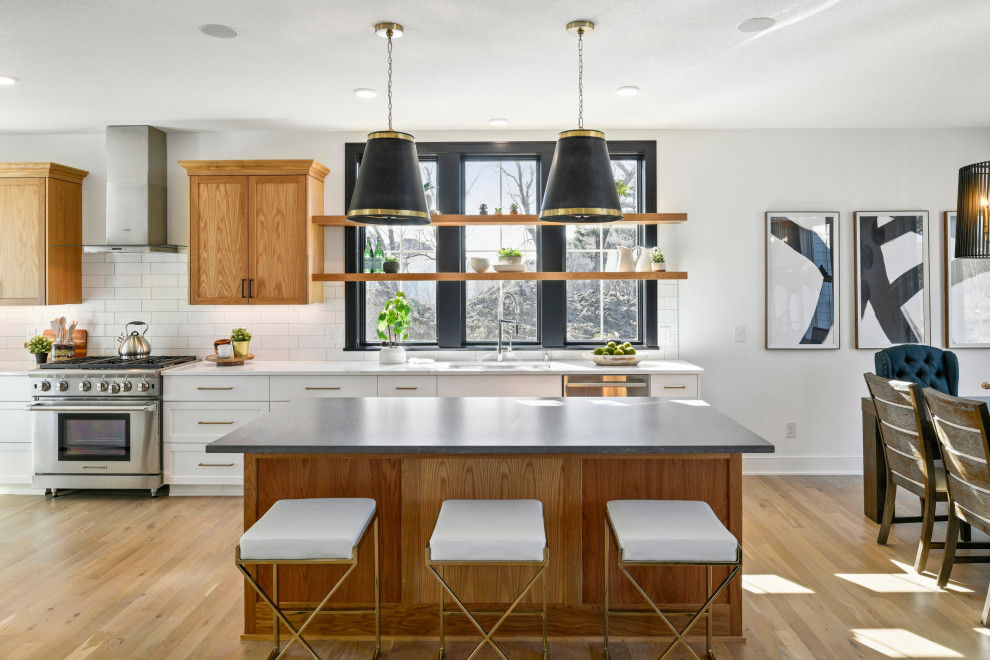 Photo of a mid-sized transitional galley eat-in kitchen in Minneapolis with a drop-in sink, recessed-panel cabinets, light wood cabinets, quartz benchtops, white splashback, ceramic splashback, stainless steel appliances, light hardwood floors, with island, brown floor and white benchtop.