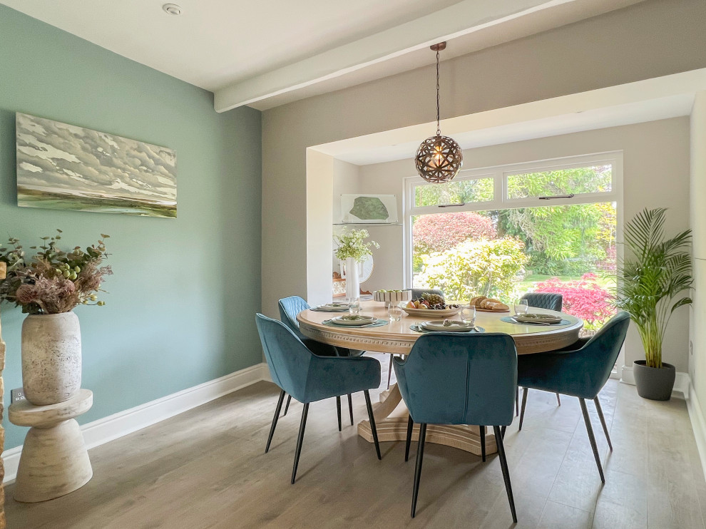 Cette photo montre une grande salle à manger ouverte sur la cuisine nature avec un mur vert, un sol en vinyl, un poêle à bois, un manteau de cheminée en pierre et poutres apparentes.