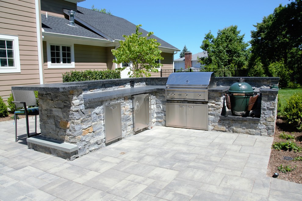 This is an example of a large tropical backyard patio in New York with an outdoor kitchen, natural stone pavers and no cover.