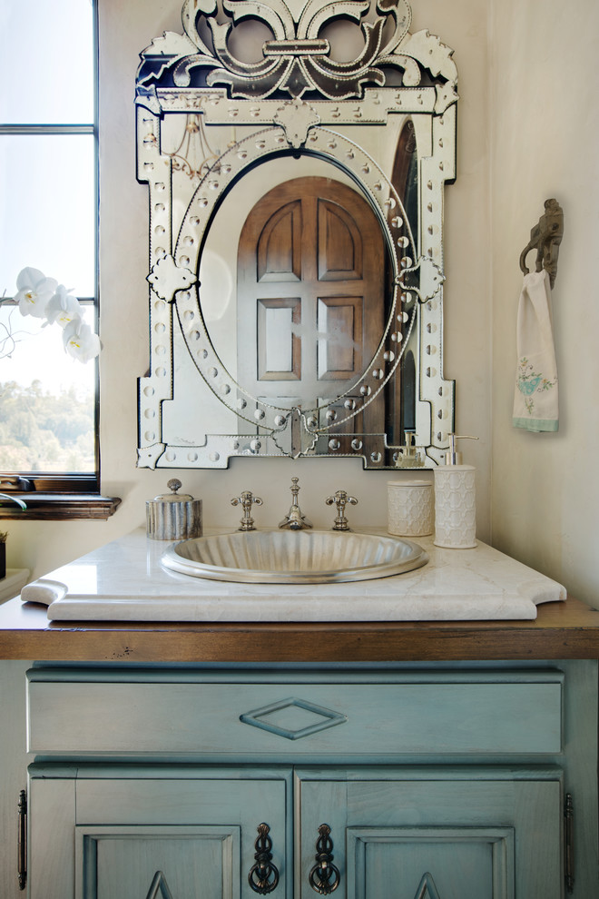 This is an example of a mediterranean powder room in Other with furniture-like cabinets, blue cabinets, beige walls, a drop-in sink, wood benchtops, a two-piece toilet, dark hardwood floors and brown floor.