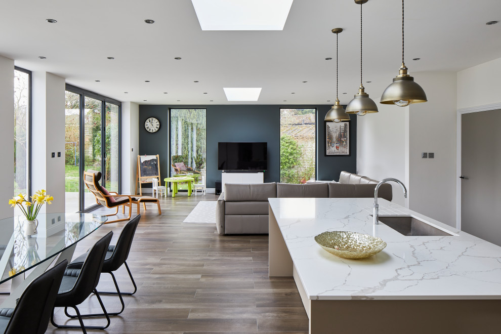 Inspiration for a mid-sized contemporary l-shaped open plan kitchen in London with a drop-in sink, flat-panel cabinets, beige cabinets, marble benchtops, white splashback, dark hardwood floors, with island, brown floor and white benchtop.