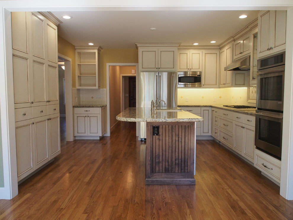 This is an example of a traditional l-shaped open plan kitchen in San Francisco with an undermount sink, flat-panel cabinets, beige cabinets, granite benchtops, yellow splashback, porcelain splashback, stainless steel appliances, medium hardwood floors, with island and multi-coloured benchtop.