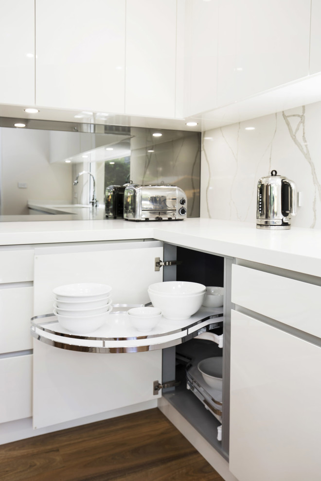 Mid-sized modern l-shaped eat-in kitchen in Sydney with an undermount sink, flat-panel cabinets, white cabinets, quartz benchtops, metallic splashback, mirror splashback, white appliances, medium hardwood floors and with island.