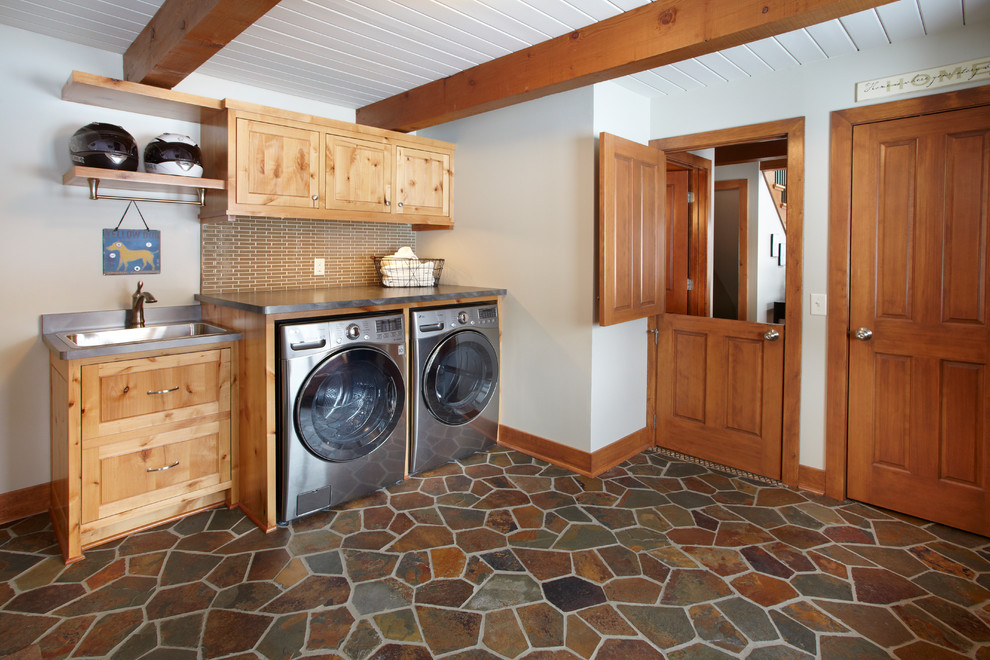 This is an example of a large transitional single-wall utility room in Minneapolis with an utility sink, flat-panel cabinets, light wood cabinets, laminate benchtops, white walls, slate floors and a side-by-side washer and dryer.