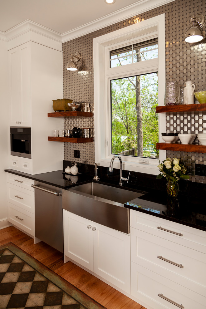 Enclosed kitchen - mid-sized transitional l-shaped enclosed kitchen idea with shaker cabinets, white cabinets, stainless steel appliances, an island and black countertops