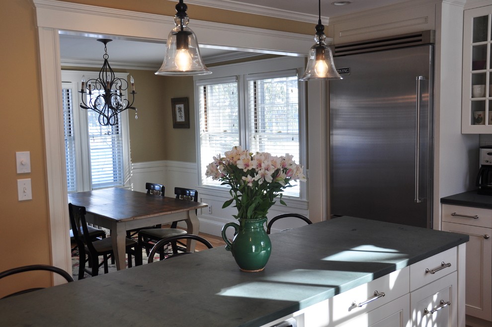 Example of a mid-sized transitional l-shaped medium tone wood floor eat-in kitchen design in Boston with a drop-in sink, glass-front cabinets, white cabinets, limestone countertops, white backsplash, subway tile backsplash, stainless steel appliances and an island