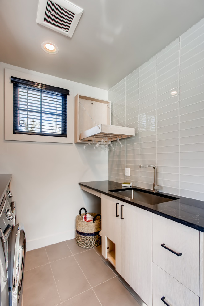 Photo of a contemporary dedicated laundry room in Denver with flat-panel cabinets, beige cabinets, black benchtop, an undermount sink, white walls, a side-by-side washer and dryer and beige floor.