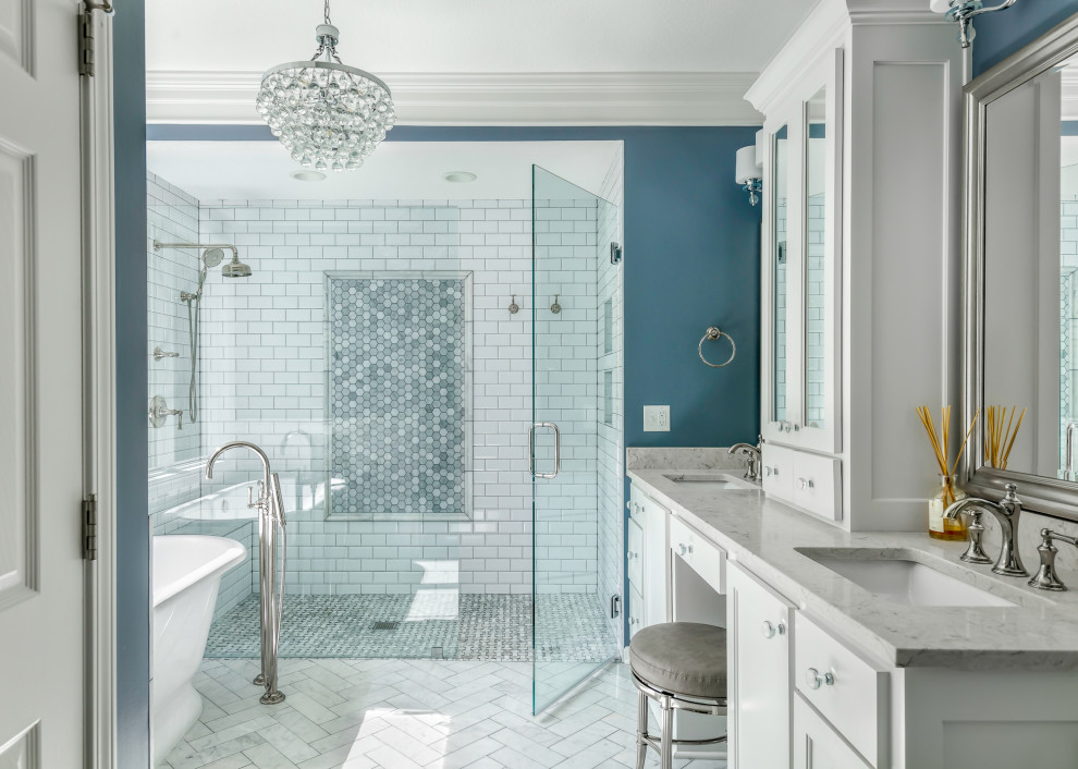 Стильный дизайн: главная ванная комната среднего размера в стиле неоклассика (современная классика) с белыми фасадами, отдельно стоящей ванной, душем без бортиков, раздельным унитазом, белой плиткой, керамогранитной плиткой, синими стенами, полом из керамогранита, врезной раковиной, столешницей из искусственного кварца, разноцветным полом, душем с распашными дверями, серой столешницей, сиденьем для душа, тумбой под две раковины, встроенной тумбой и фасадами в стиле шейкер - последний тренд