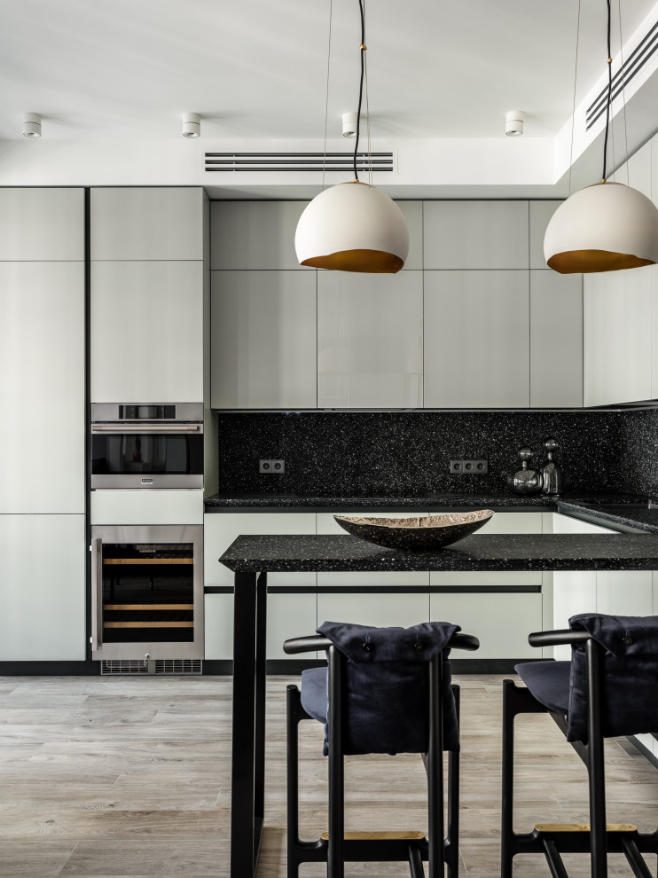 This is an example of a mid-sized contemporary l-shaped eat-in kitchen in Moscow with an undermount sink, flat-panel cabinets, grey cabinets, quartzite benchtops, black splashback, engineered quartz splashback, stainless steel appliances, porcelain floors, grey floor and black benchtop.