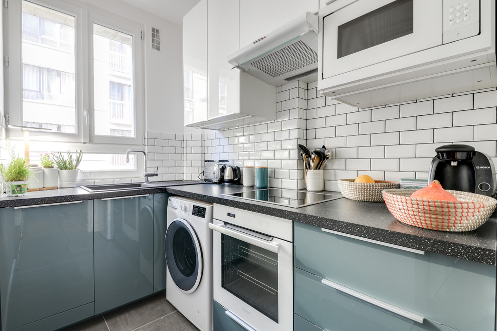 Photo of a small contemporary l-shaped kitchen in Paris with a drop-in sink, flat-panel cabinets, blue cabinets, white splashback, subway tile splashback, white appliances, no island, grey floor, laminate benchtops, ceramic floors and black benchtop.