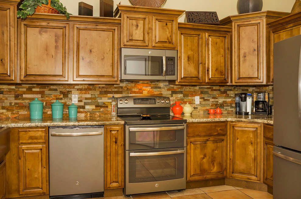 This is an example of a mid-sized country u-shaped eat-in kitchen in Phoenix with a farmhouse sink, raised-panel cabinets, medium wood cabinets, granite benchtops, orange splashback, stone tile splashback, stainless steel appliances, porcelain floors and no island.