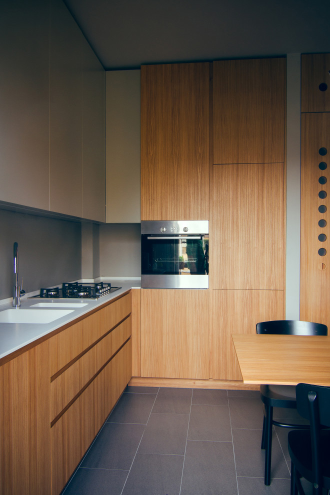 This is an example of a mid-sized contemporary l-shaped eat-in kitchen with an integrated sink, flat-panel cabinets, light wood cabinets, solid surface benchtops, grey splashback, stainless steel appliances, limestone floors, no island and grey floor.