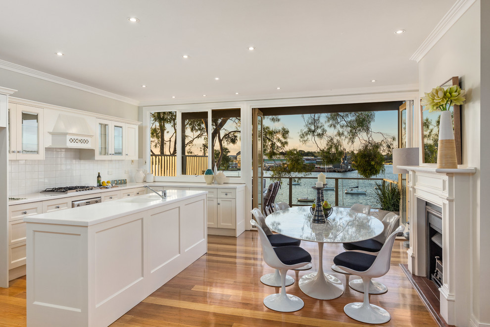 Photo of a mid-sized contemporary single-wall eat-in kitchen in Sydney with a double-bowl sink, recessed-panel cabinets, white cabinets, terrazzo benchtops, white splashback, ceramic splashback, stainless steel appliances, medium hardwood floors and with island.