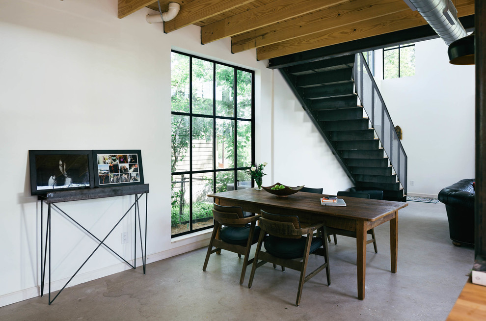 This is an example of an industrial open plan dining in Austin with white walls and concrete floors.