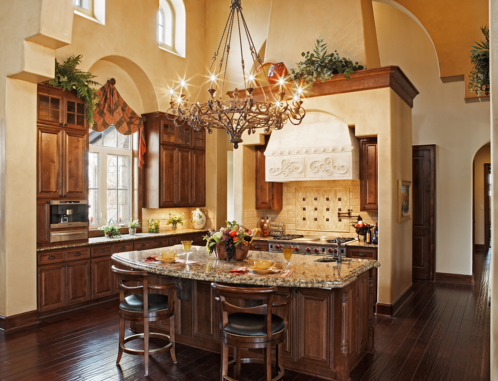 This is an example of a large mediterranean l-shaped kitchen in Austin with raised-panel cabinets, dark wood cabinets, granite benchtops, beige splashback, subway tile splashback, dark hardwood floors, with island and brown floor.