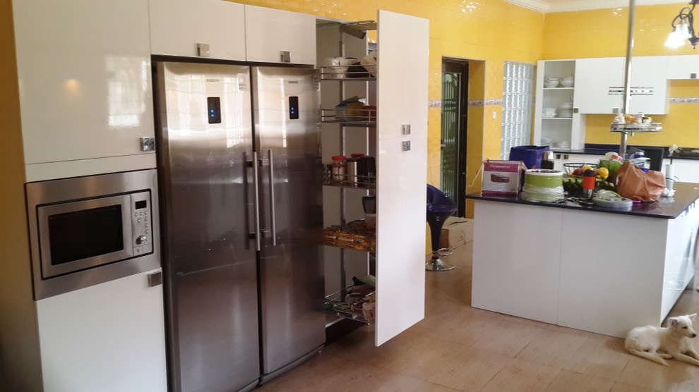 Photo of a large modern u-shaped eat-in kitchen in Other with a double-bowl sink, flat-panel cabinets, white cabinets, quartzite benchtops, yellow splashback, ceramic splashback, coloured appliances, porcelain floors and with island.