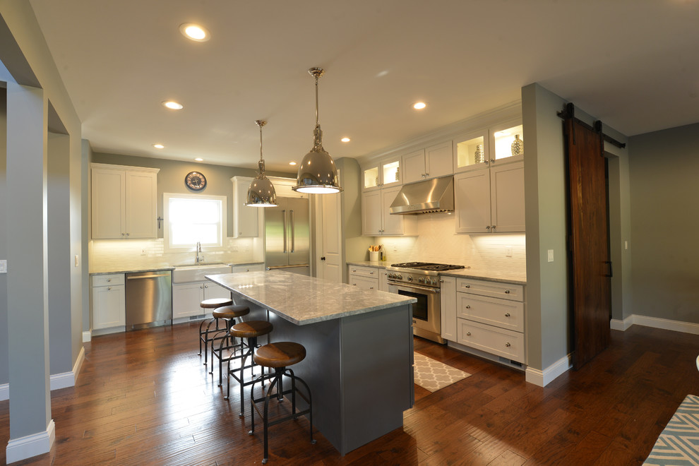 Large transitional l-shaped dark wood floor and brown floor eat-in kitchen photo in St Louis with a farmhouse sink, shaker cabinets, white cabinets, granite countertops, white backsplash, subway tile backsplash, stainless steel appliances, an island and gray countertops