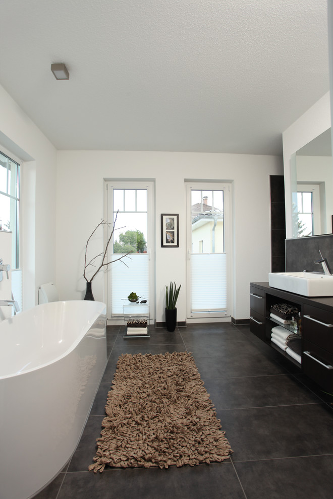Photo of a large contemporary bathroom in Other with black cabinets, a freestanding tub, gray tile, white walls, a vessel sink, flat-panel cabinets, a curbless shower, black floor and an open shower.