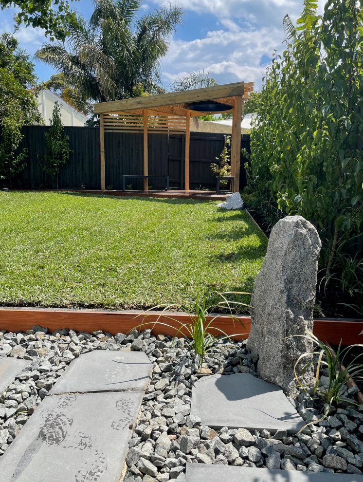 This is an example of a mid-sized asian backyard full sun formal garden for fall in Melbourne with natural stone pavers and a metal fence.