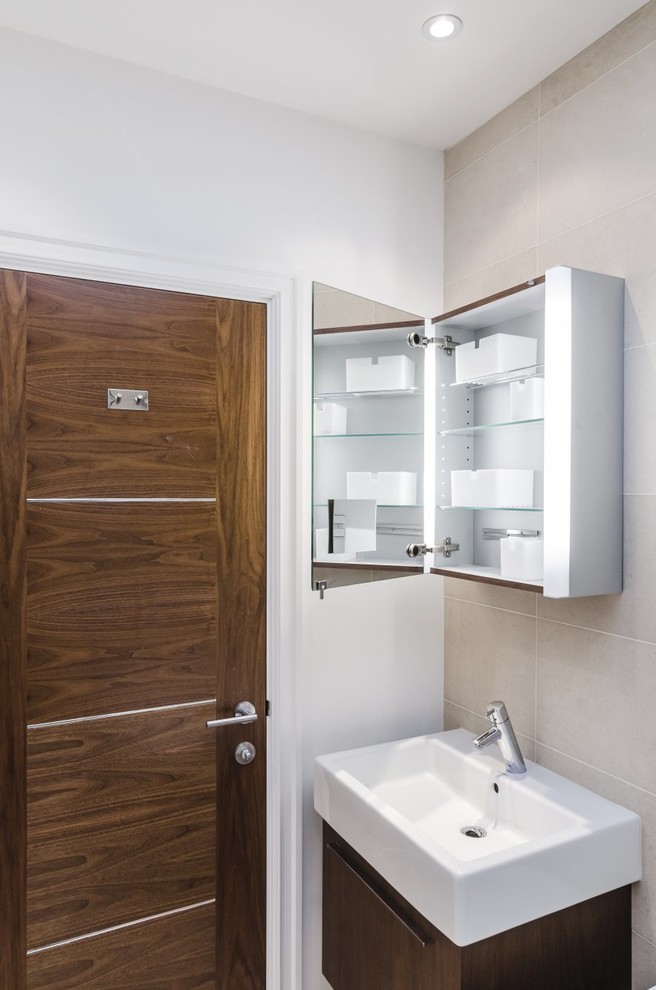 This is an example of a mid-sized modern master bathroom in London with a wall-mount sink, flat-panel cabinets, dark wood cabinets, a drop-in tub, a shower/bathtub combo, a wall-mount toilet, beige tile, porcelain tile, beige walls and porcelain floors.