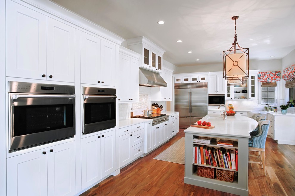 Mid-sized transitional u-shaped medium tone wood floor and brown floor enclosed kitchen photo in Denver with a farmhouse sink, shaker cabinets, white cabinets, quartzite countertops, gray backsplash, marble backsplash, stainless steel appliances and an island
