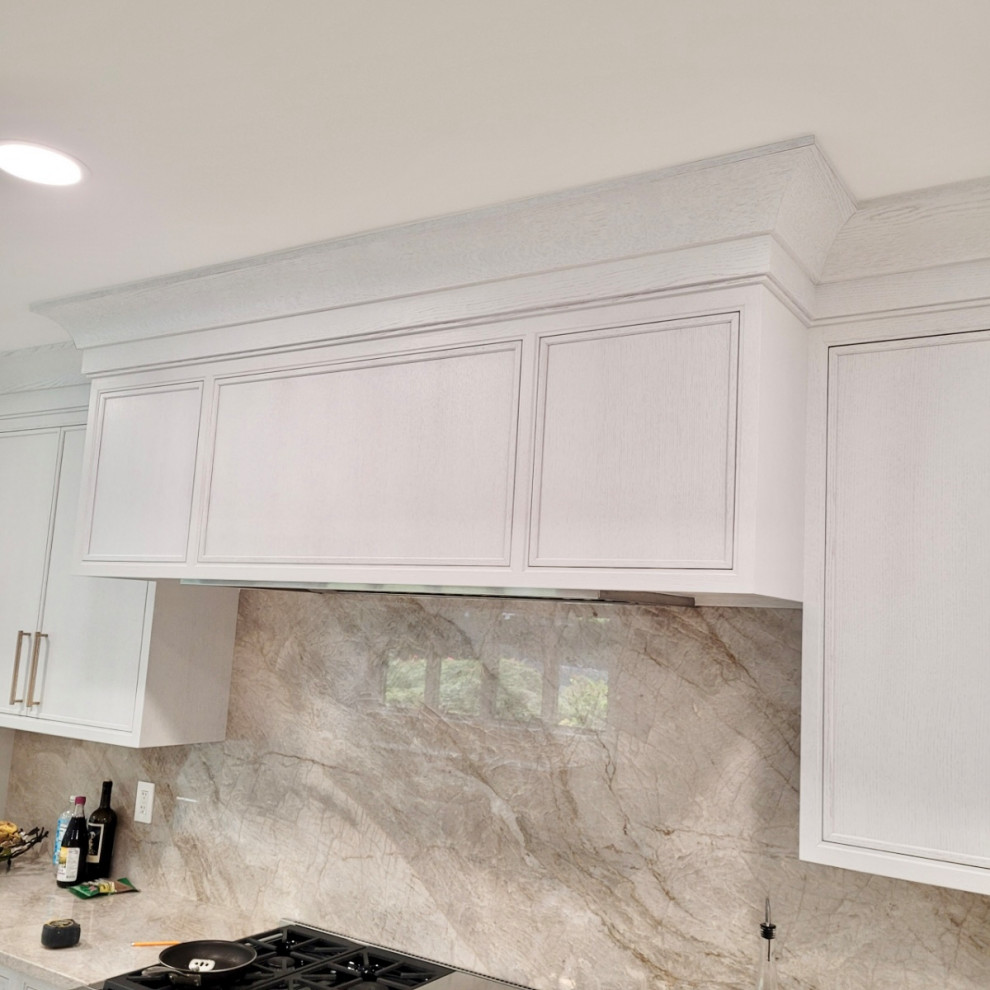Photo of a large classic u-shaped kitchen pantry in New York with recessed-panel cabinets, white cabinets, quartz worktops, beige splashback, stone slab splashback, integrated appliances, an island, beige worktops, a submerged sink, porcelain flooring and beige floors.