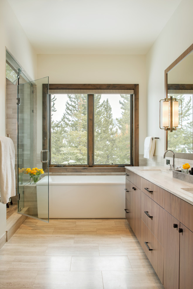 Example of a mountain style master beige floor and double-sink freestanding bathtub design with flat-panel cabinets, medium tone wood cabinets, white walls, an undermount sink, a hinged shower door and white countertops