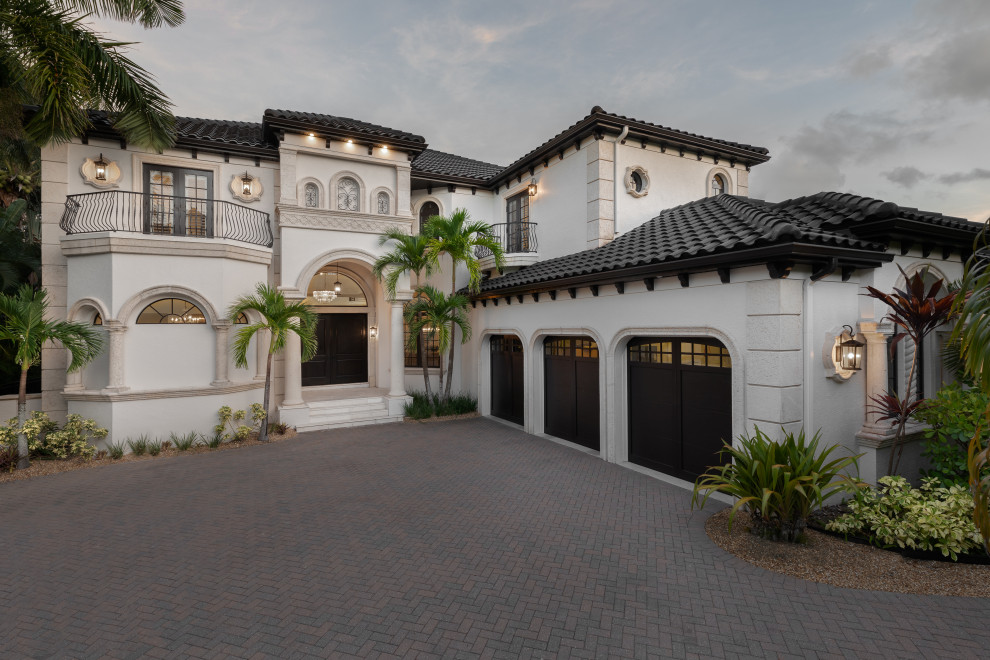 This is an example of a mediterranean two-storey white house exterior in Tampa with a gable roof, a tile roof and a black roof.