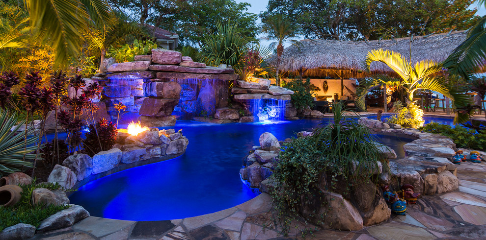 Inspiration for an expansive tropical backyard custom-shaped natural pool in Tampa with a water feature and natural stone pavers.