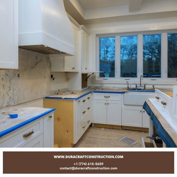 Example of a mid-sized u-shaped laminate floor, beige floor and tray ceiling eat-in kitchen design with a farmhouse sink, white cabinets, marble countertops, beige backsplash, marble backsplash, stainless steel appliances, an island and beige countertops