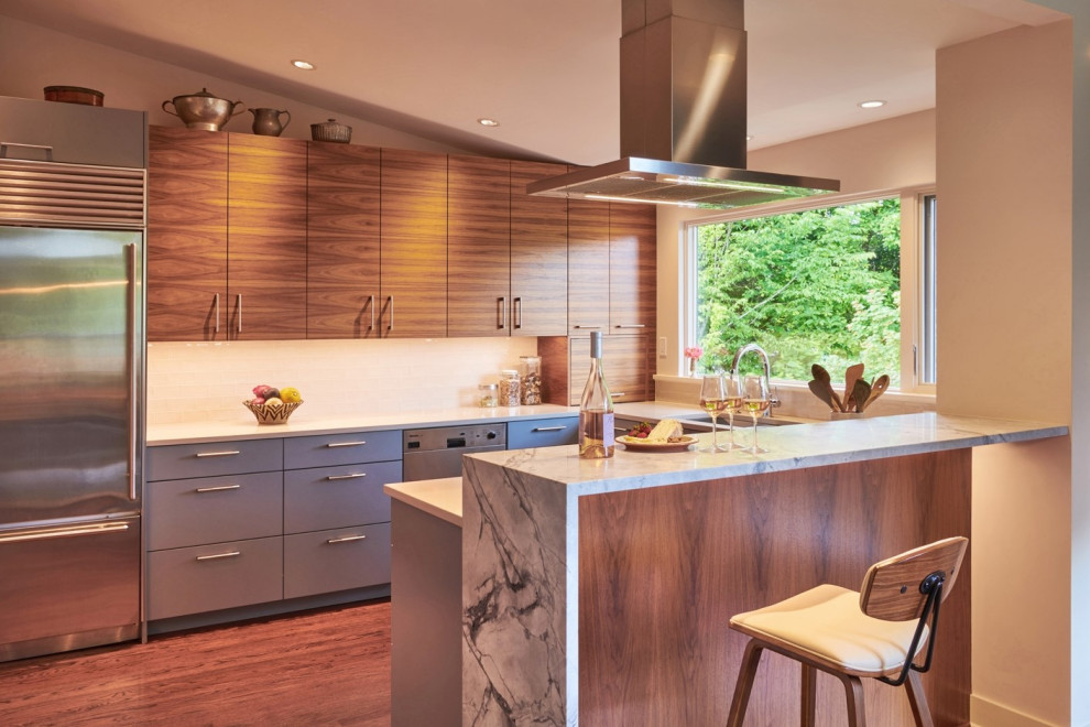 Photo of a mid-sized midcentury u-shaped eat-in kitchen in Seattle with an undermount sink, flat-panel cabinets, medium wood cabinets, solid surface benchtops, white splashback, ceramic splashback, stainless steel appliances, dark hardwood floors, a peninsula, brown floor, white benchtop and vaulted.