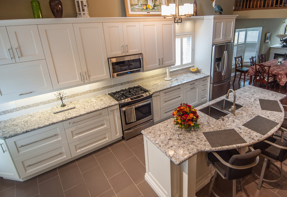 Inspiration for a mid-sized transitional galley ceramic tile eat-in kitchen remodel in Toronto with a double-bowl sink, shaker cabinets, white cabinets, granite countertops, beige backsplash, stone tile backsplash, stainless steel appliances and an island