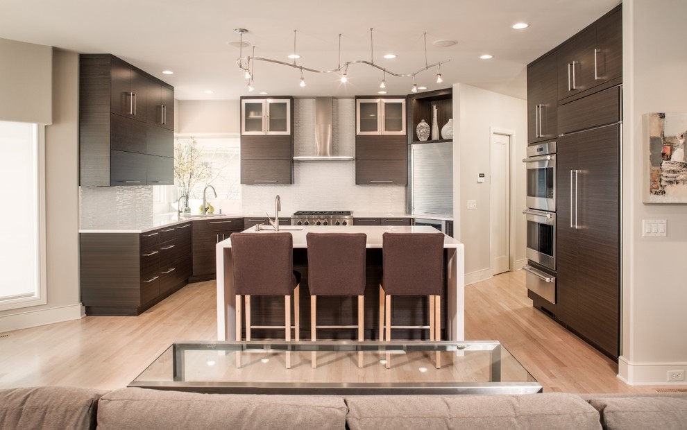 Mid-sized transitional u-shaped light wood floor eat-in kitchen photo in Omaha with an island, an undermount sink, flat-panel cabinets, brown cabinets, quartz countertops, white backsplash, glass sheet backsplash and stainless steel appliances